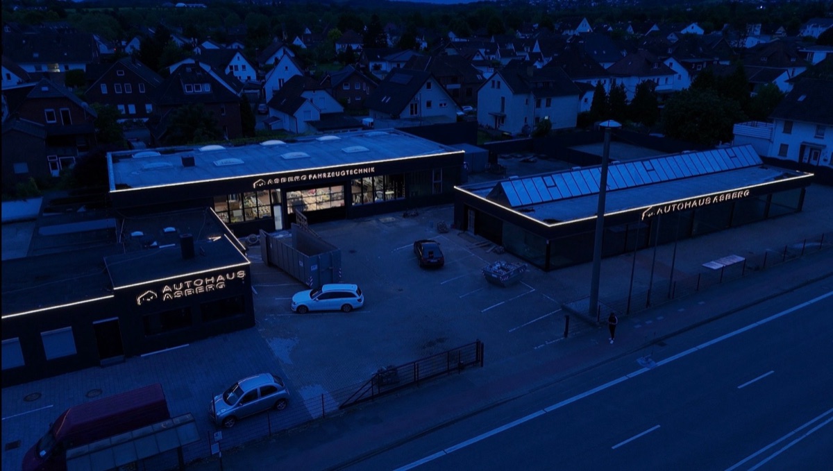 Autohaus Asberg bei Nacht aus der Luft: Leuchtbuchstaben und LED-Lichtlinien an zwei Gebäuden